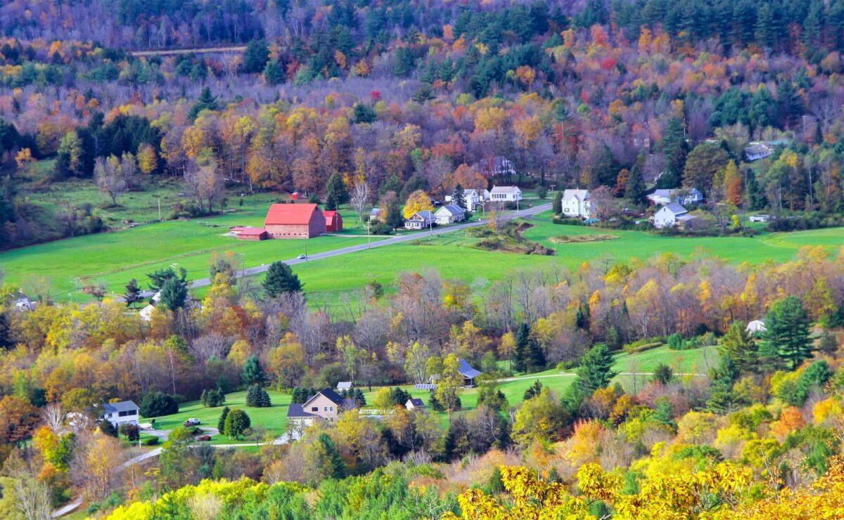 Rural homes and a red barn surrounded by colorful fall foliage in the Berkshires of western Massachusetts.