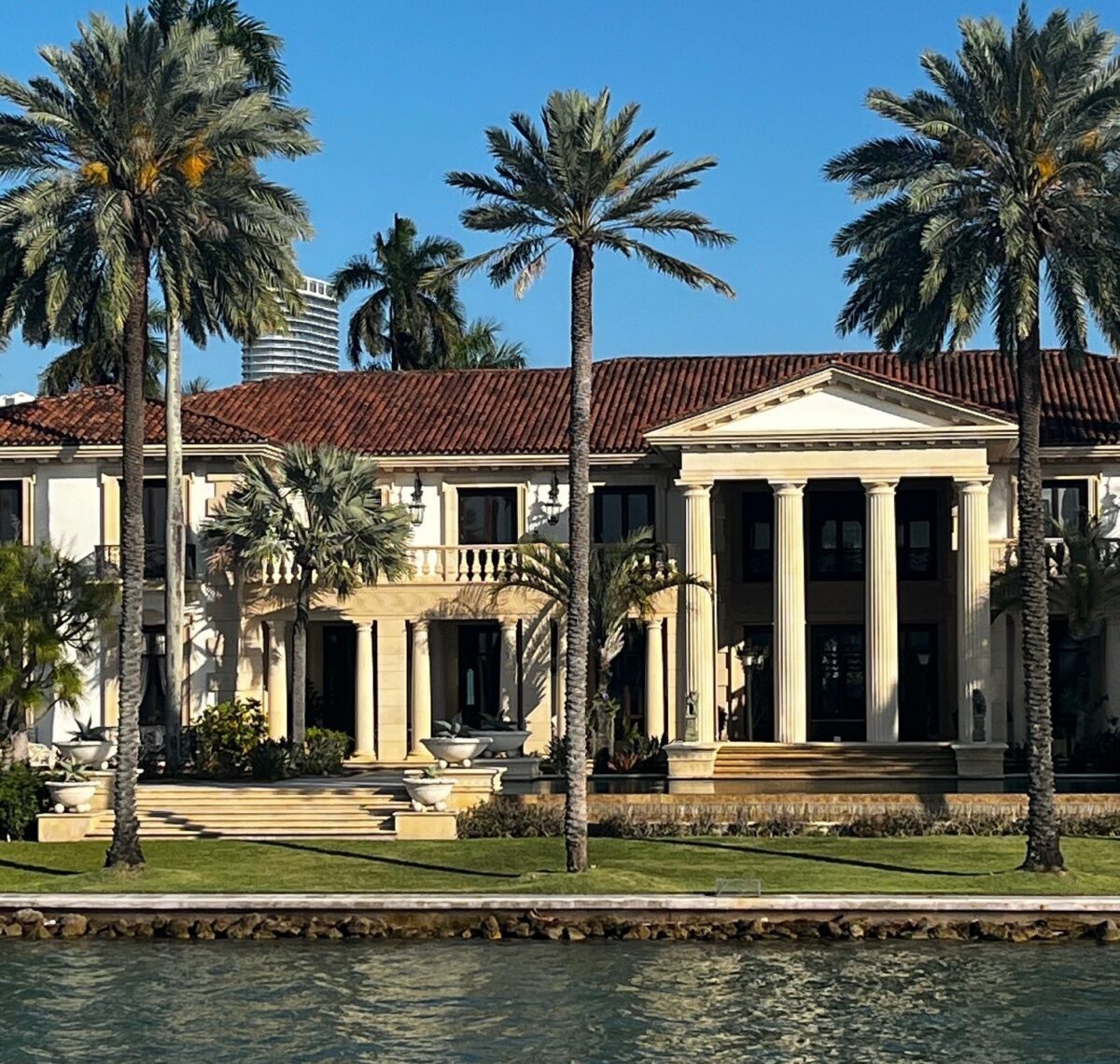 A waterfront mansion with palm trees viewed from the water