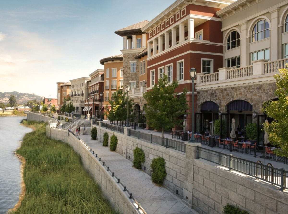Colorful buildings and outdoor dining patios overlook a paved walkway along the Napa River in downtown Napa.