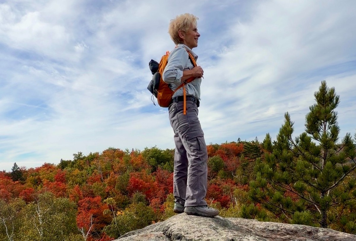 Krissie Mason standing on a rocky overlook above a forest filled with red, orange and green autumn foliage