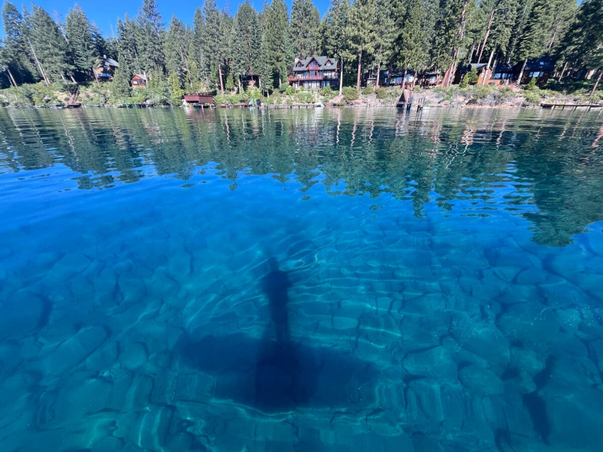 Clear turquoise water revealing rocks beneath the surface along Lake Tahoe's forested shoreline